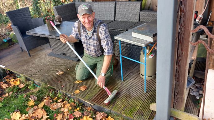 Der Aufräumer beim Reinigen einer Gartenterasse mit Holzboden